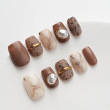 The nail art is mainly brown and off-white, dotted with pearls and gold lines