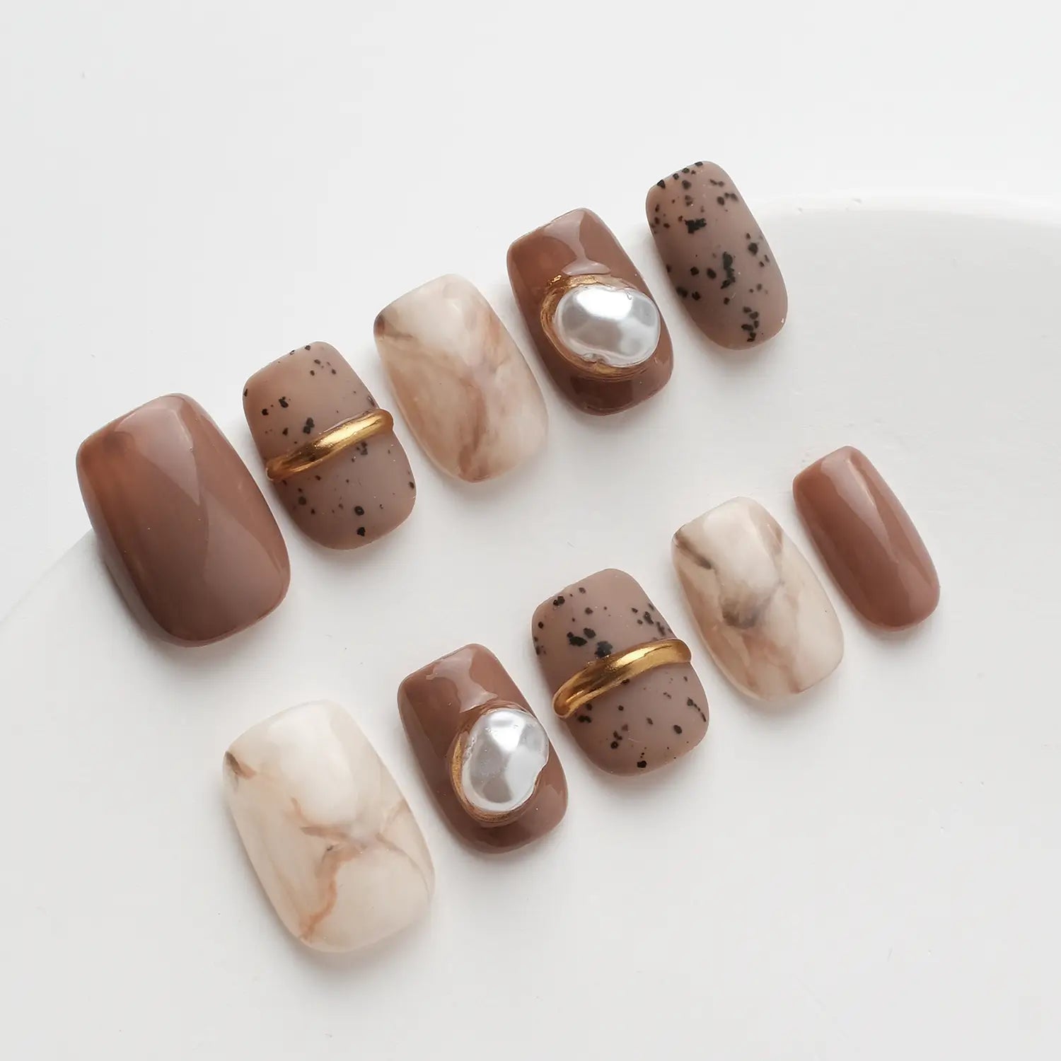 The nail art is mainly brown and off-white, dotted with pearls and gold lines