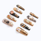 The nails feature a luxurious gold base and black and are embellished with an assortment of rhinestones