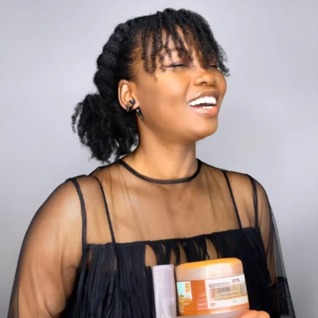 A girl with 4c hair holds a bottle of shampoo and a jar of hair gel in her hands